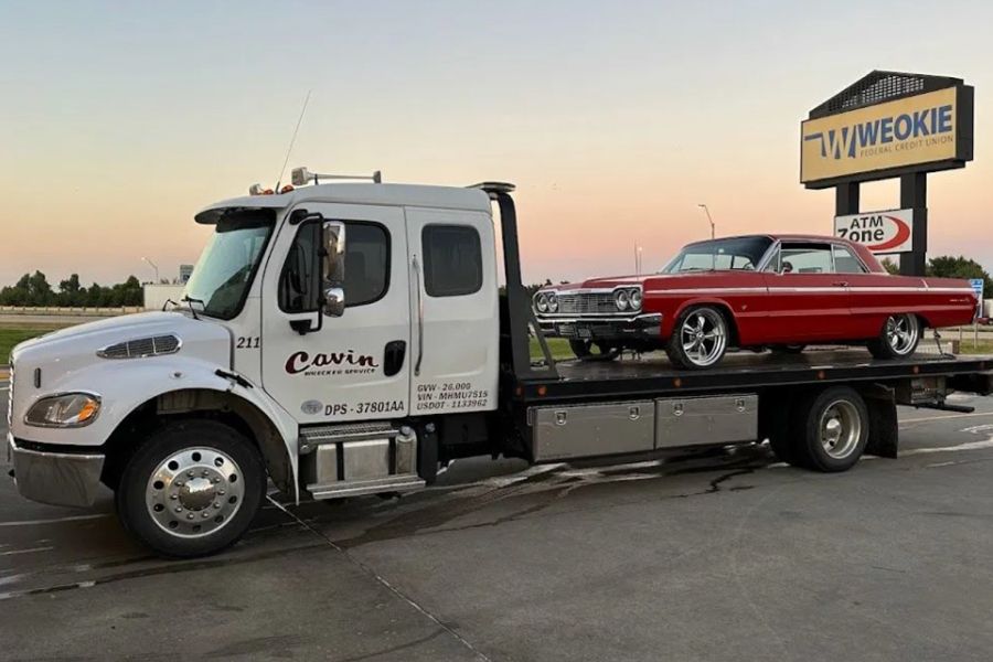 A tow truck is carrying a red car on the back of it.