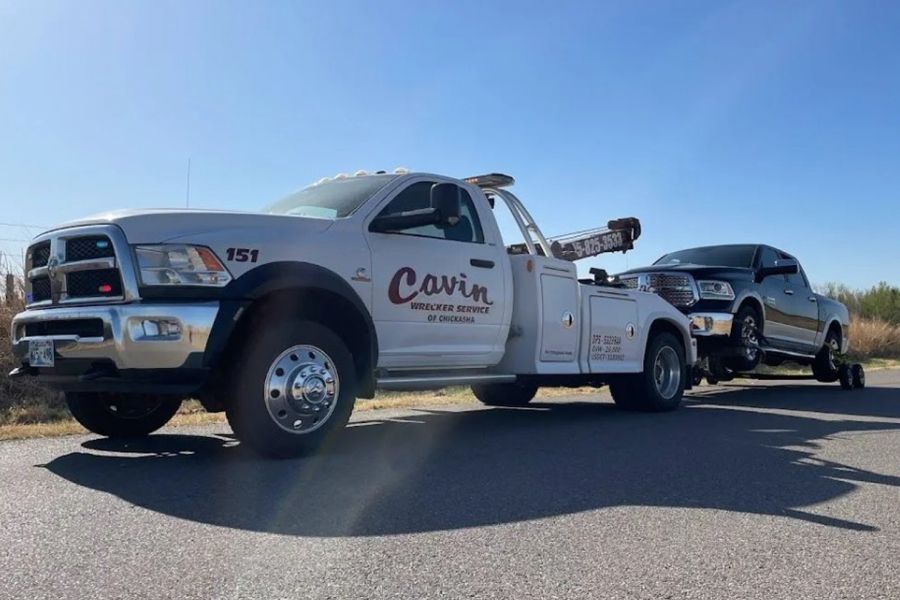 A white tow truck is towing a black car on a road.