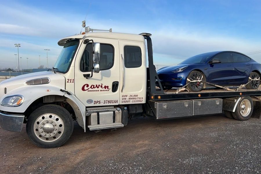 A tow truck is carrying a blue car on the back of it.