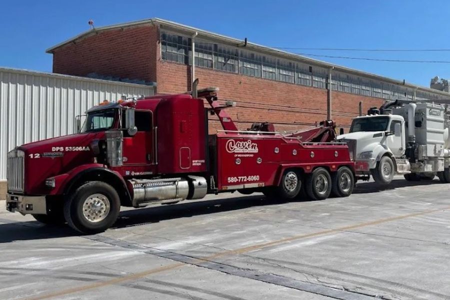 A red tow truck is parked next to a white truck in a parking lot.
