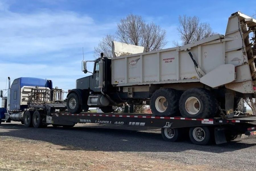 A dump truck is sitting on top of a flatbed trailer.