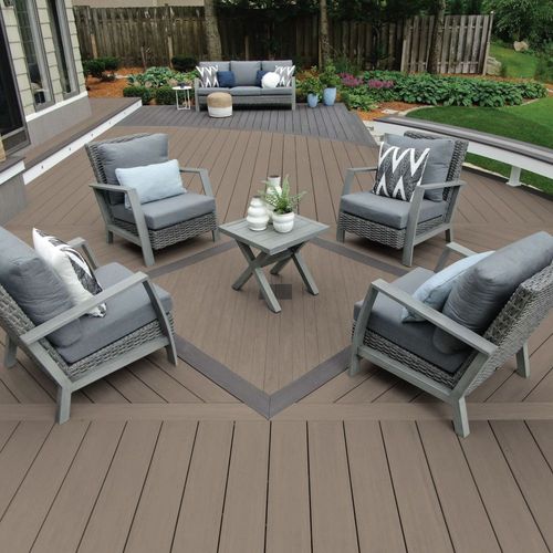Outdoor patio with gray chairs, small table, and a sofa on a wooden deck, surrounded by garden greenery.