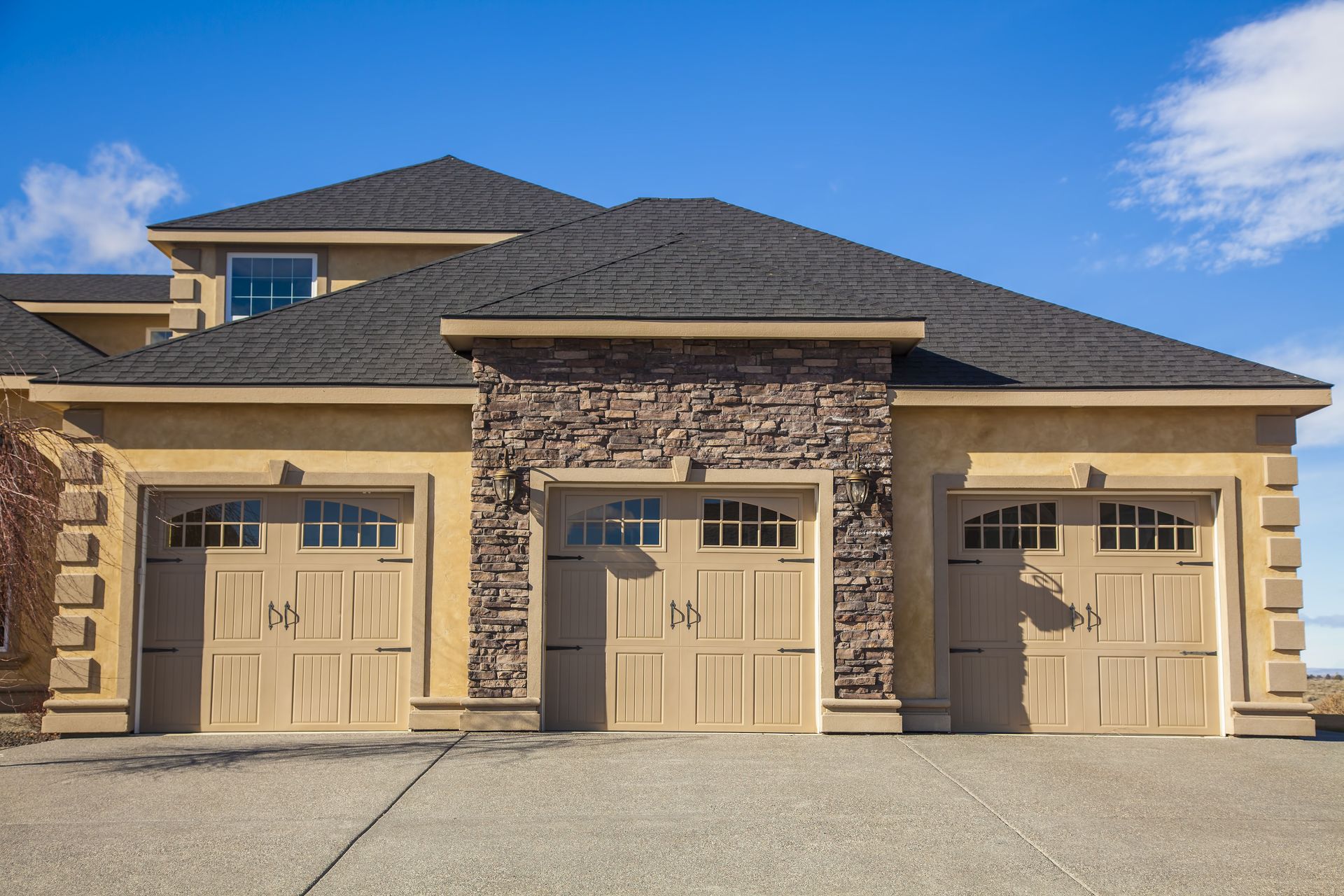 Three-car garage with tan doors and stone facade on a house under a blue sky