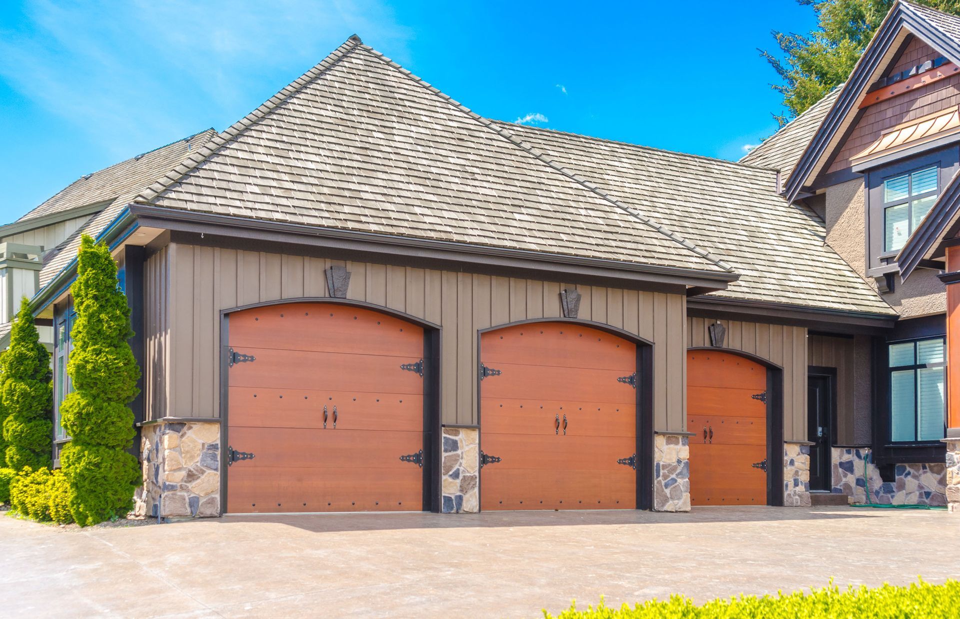Three-car garage with tan doors and stone trim on a suburban home under a bright blue sky