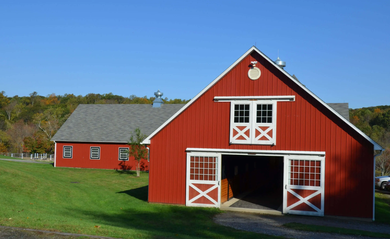 Red barn with white trim and open doors on a green lawn under a blue sky