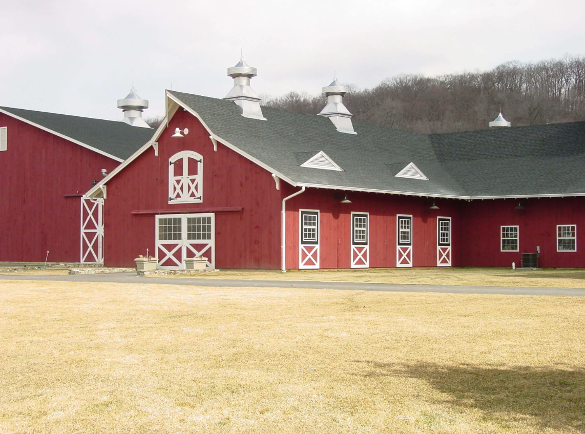 Red barn with white trim and several cupolas on a grassy field under an overcast sky