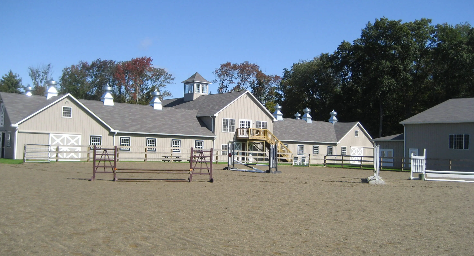 Equestrian riding arena with jumps in front of a beige stable building under a clear sky