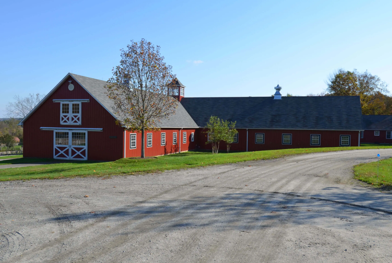 Red barn and long farmhouse beside a gravel road on a sunny rural day