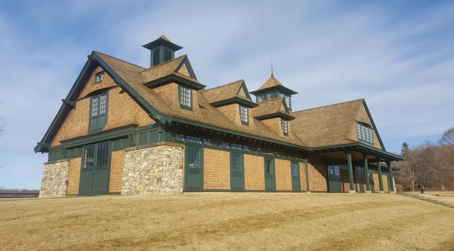 Rustic stone-and-wood lodge with a steep roof, set in a grassy field under a blue sky