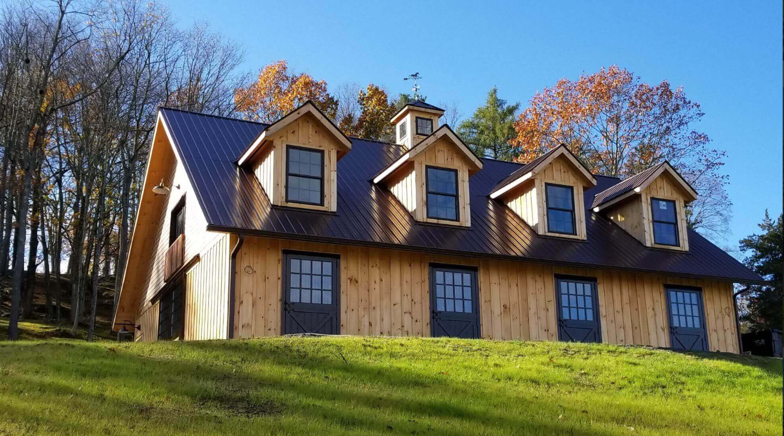 Wood-sided house with dormer windows on a grassy hill under a blue sky