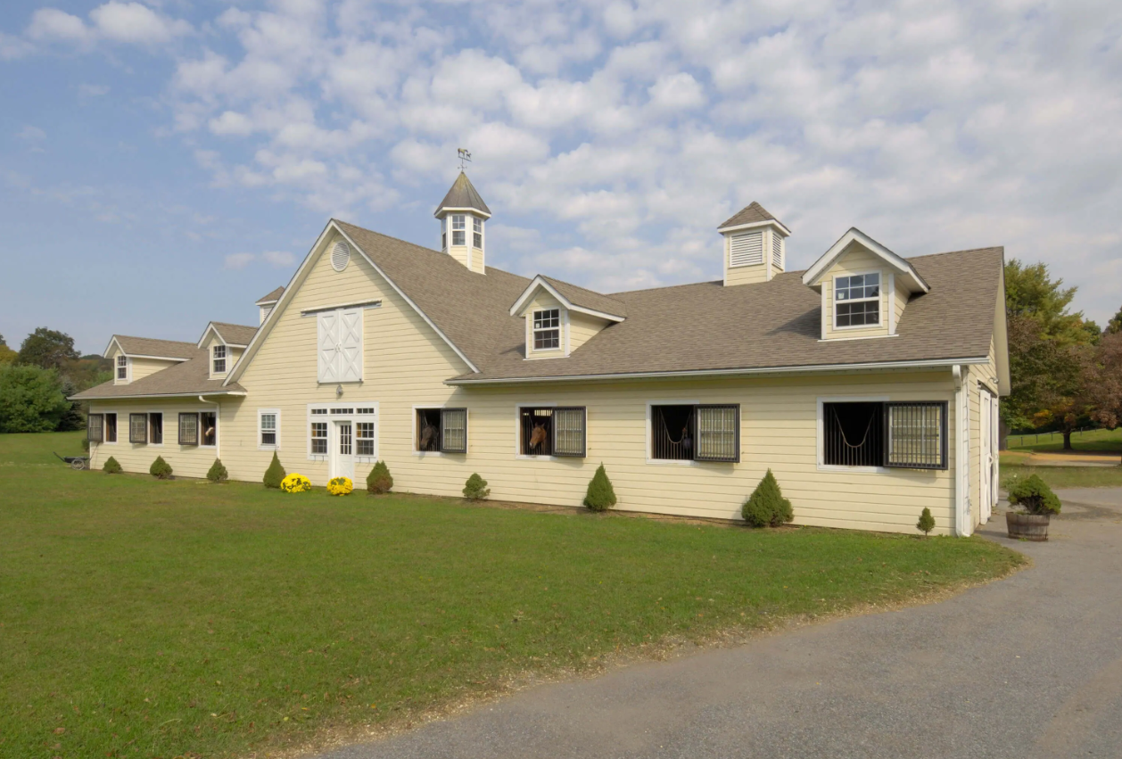 Large beige house with dormers and a wide green lawn under a cloudy sky