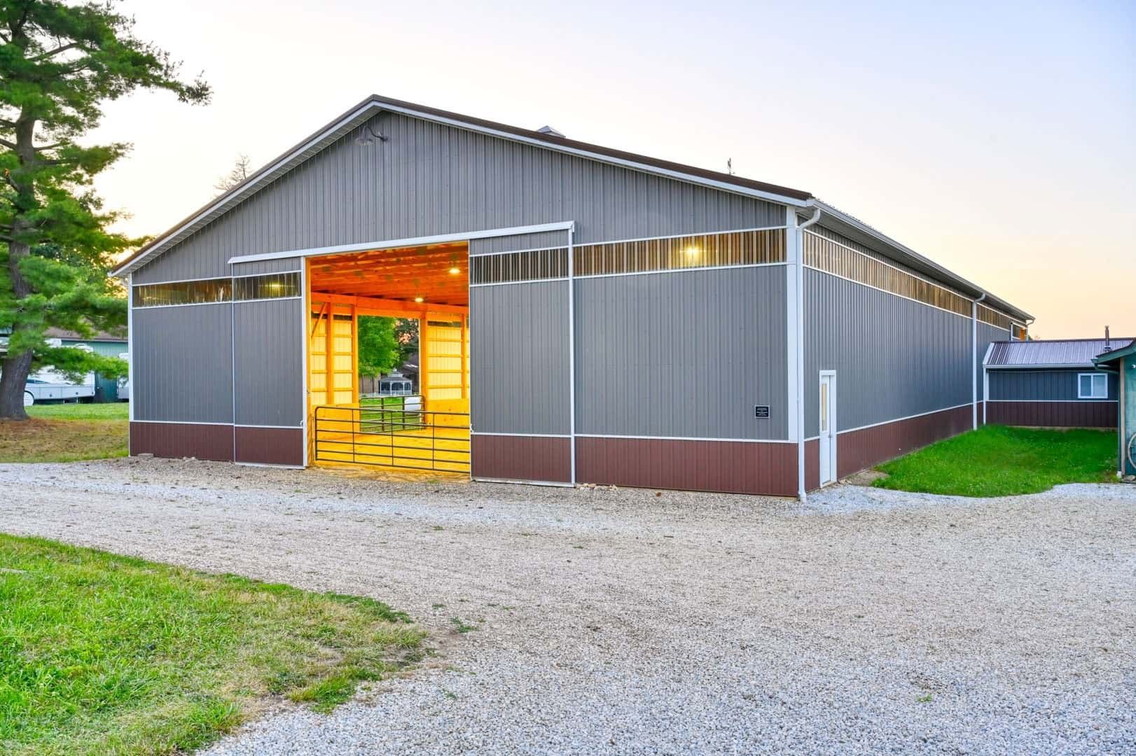 Gray barn-style building with open lit doorway on a gravel lot at sunset