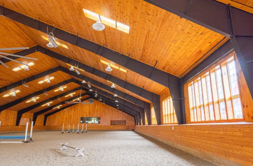 Empty indoor gym with wood-paneled ceiling, large windows, and exercise equipment along the walls