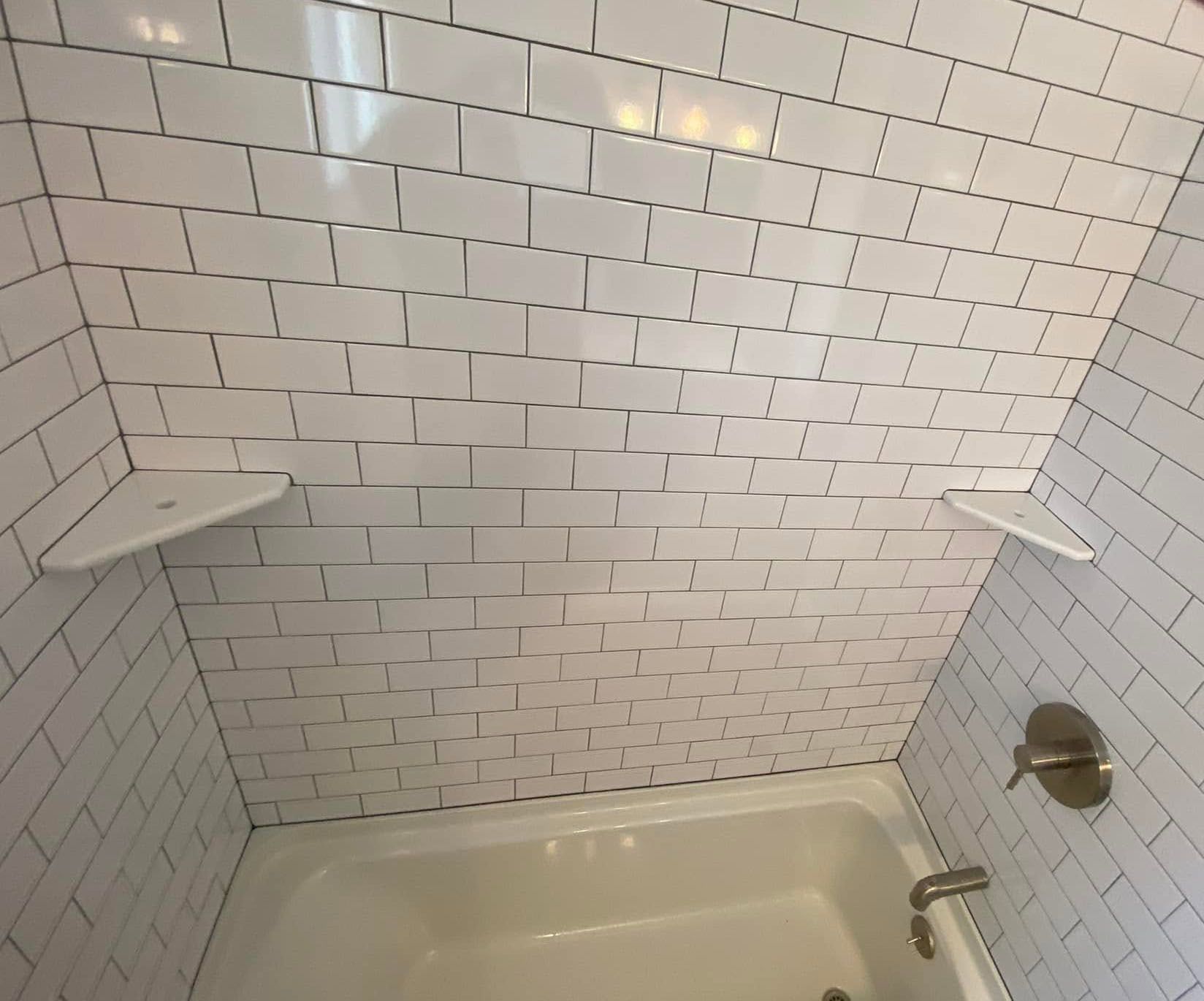 White subway-tile bathtub alcove with built-in corner shelves and chrome shower fixtures.