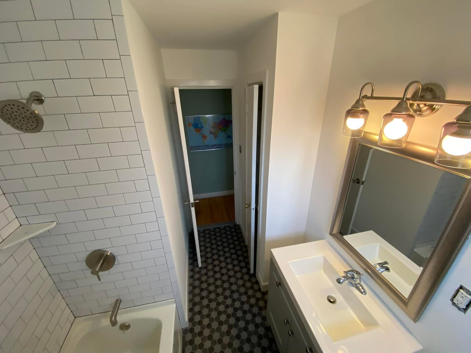 Bathroom with shower, sink, mirror, and hallway view through the open door.