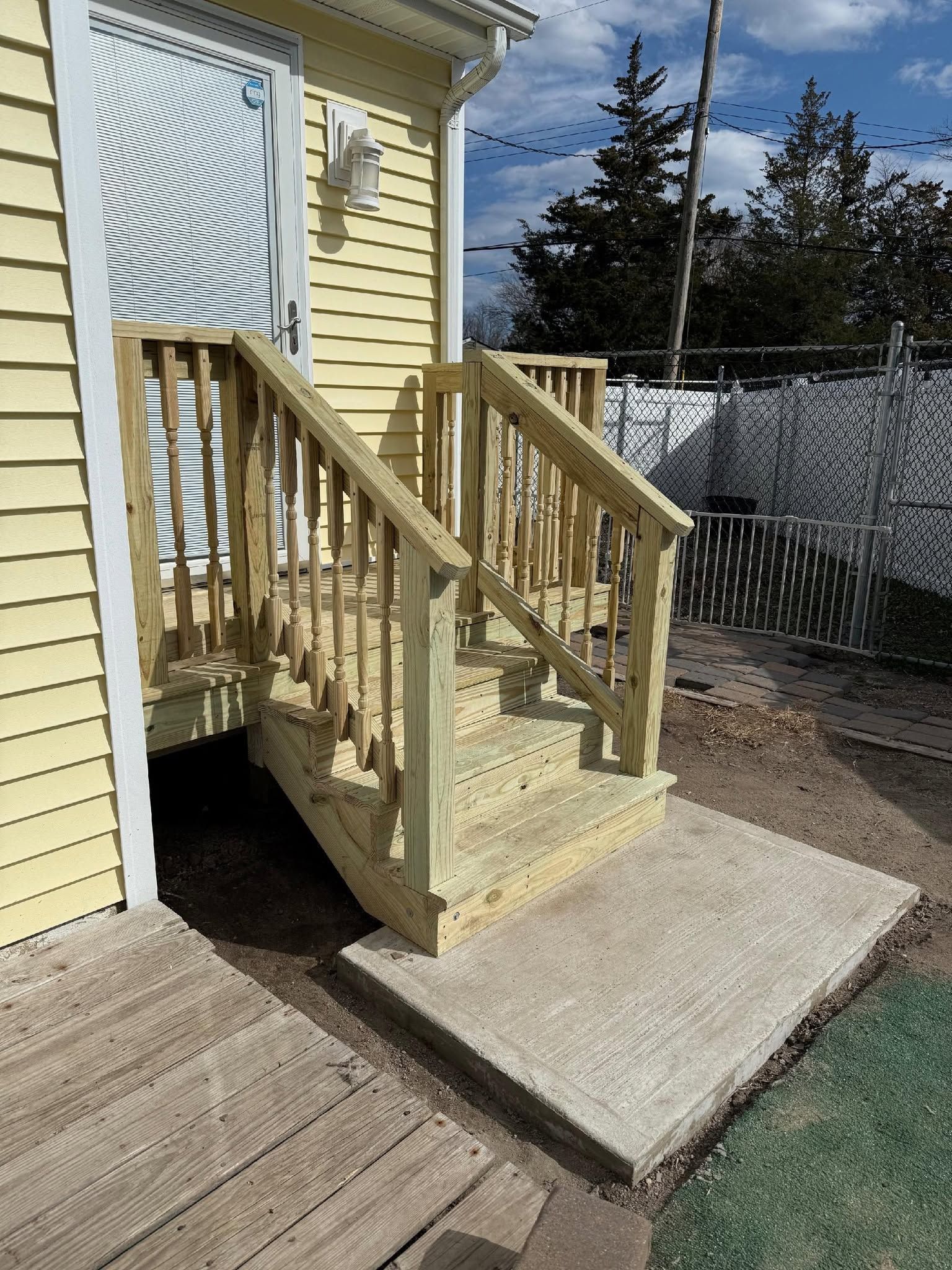 Wooden accessibility ramp and stairs leading to a house entrance, with tan siding and a concrete landing.
