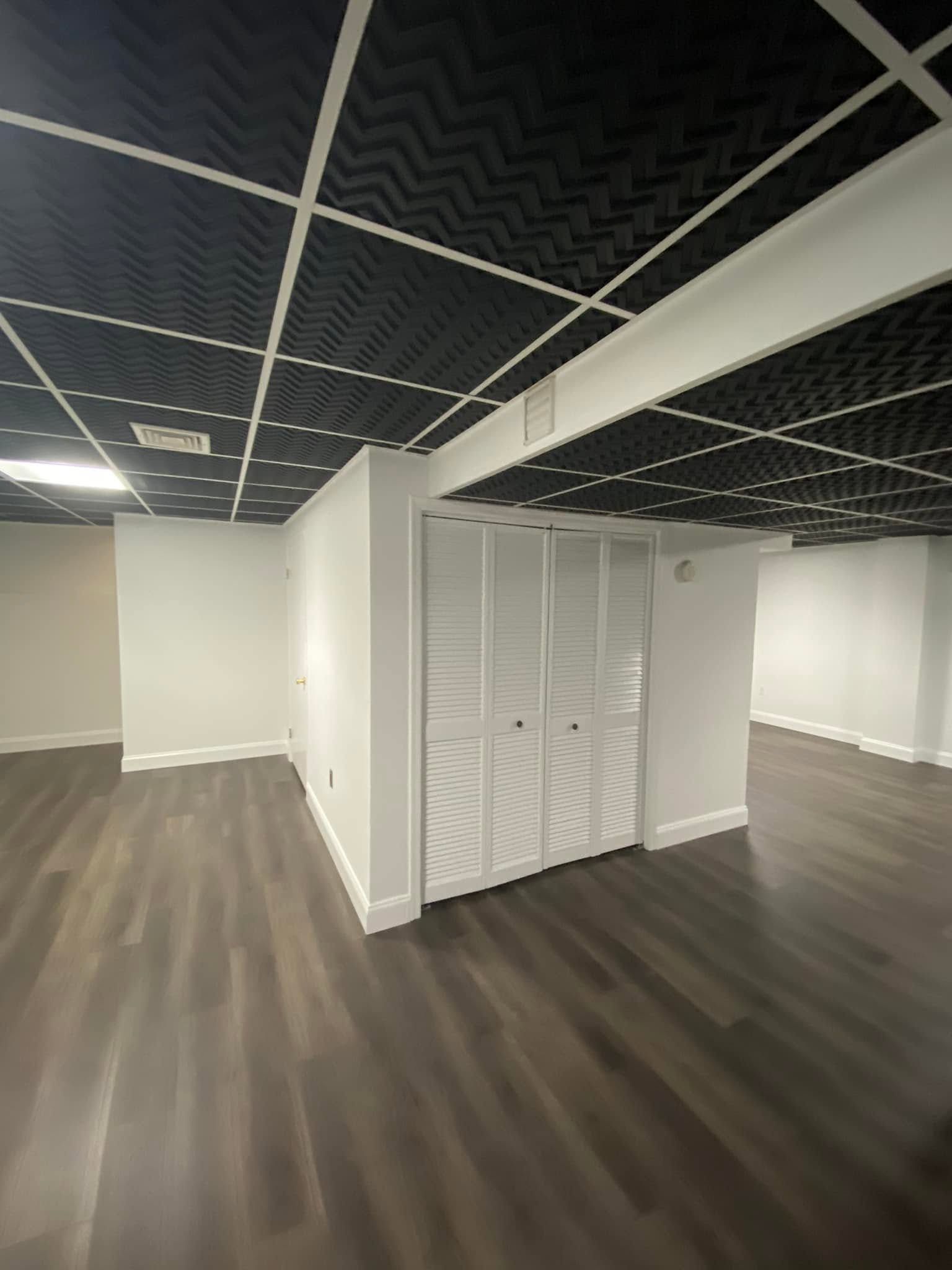Empty office space with dark wood floors, white walls, and a black grid ceiling.