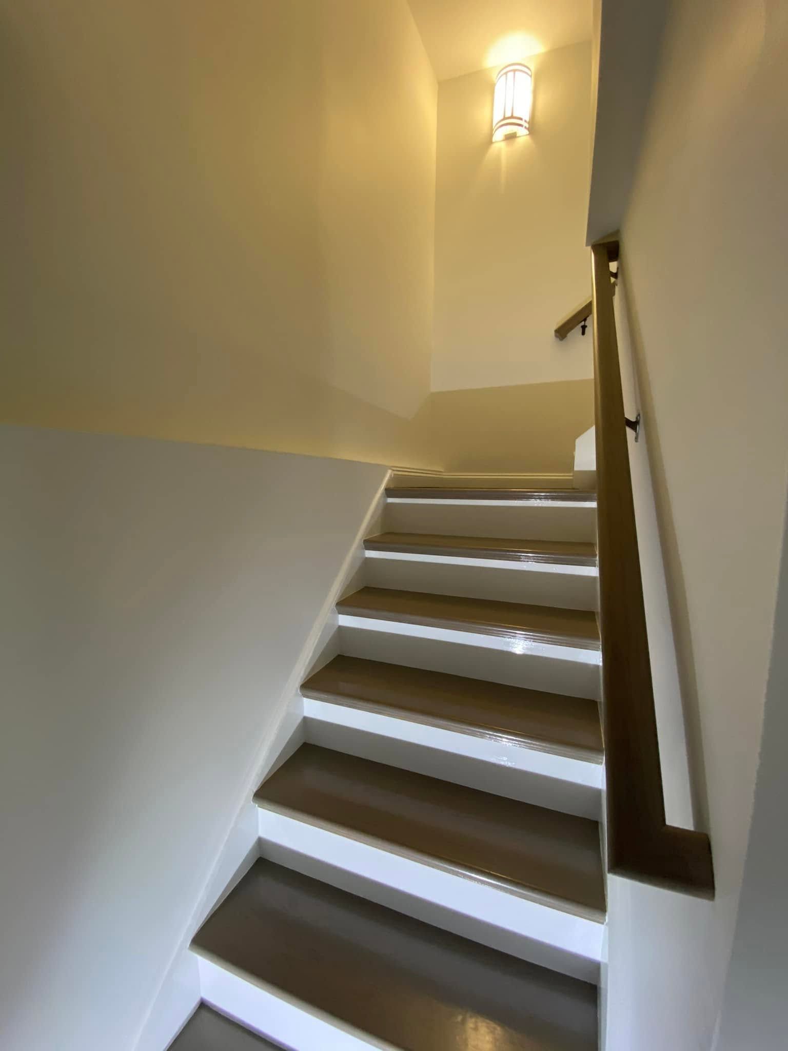 Narrow indoor staircase with white walls, dark treads, and a wall sconce at the top.
