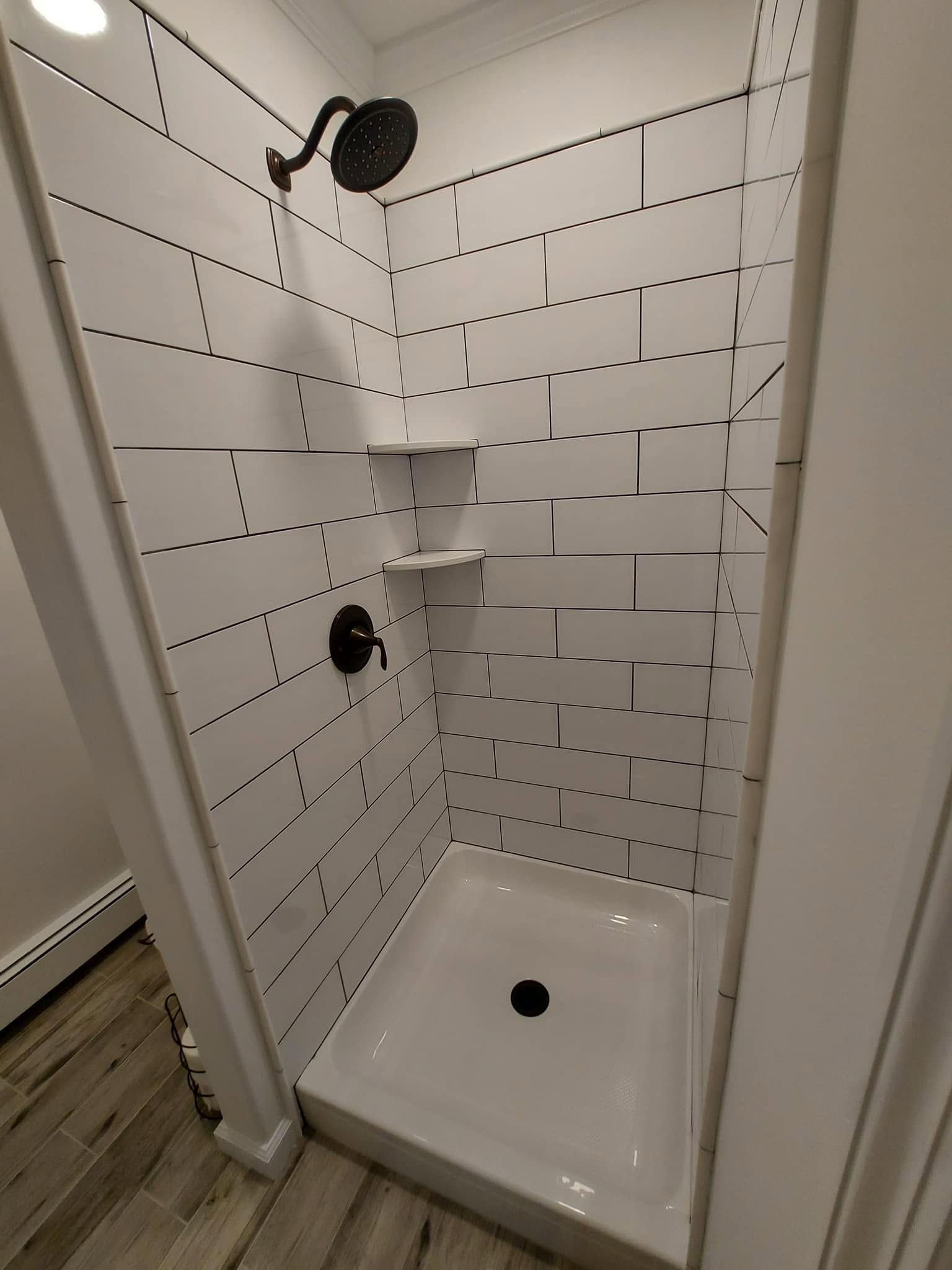 Small tiled shower stall with white walls, black fixtures, a shelf, and a built-in soap dish.