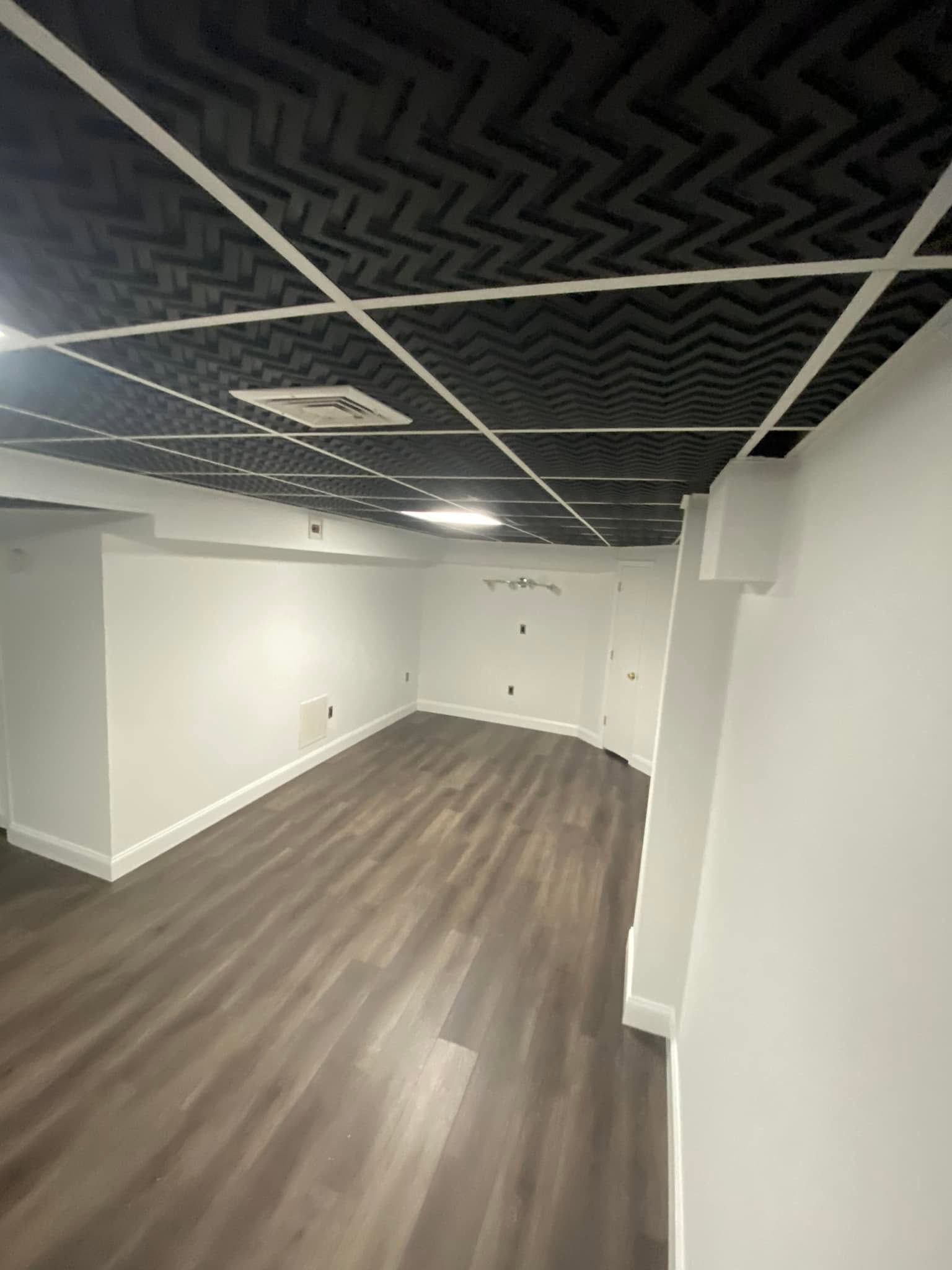 Empty office room with wood-look floor, white walls, and black acoustic ceiling panels.