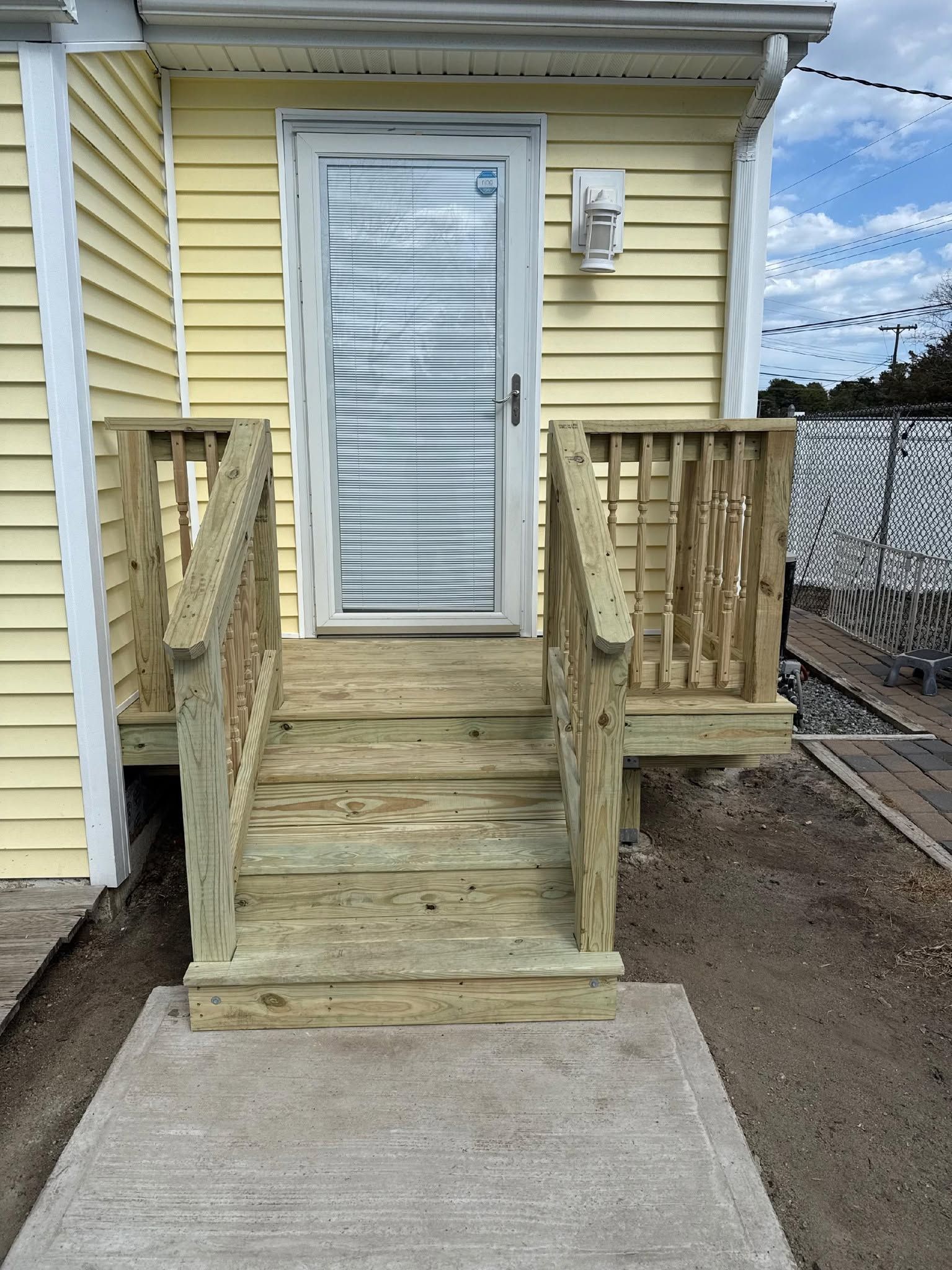 Small wooden porch with steps and railings leading to a white door on a yellow house.