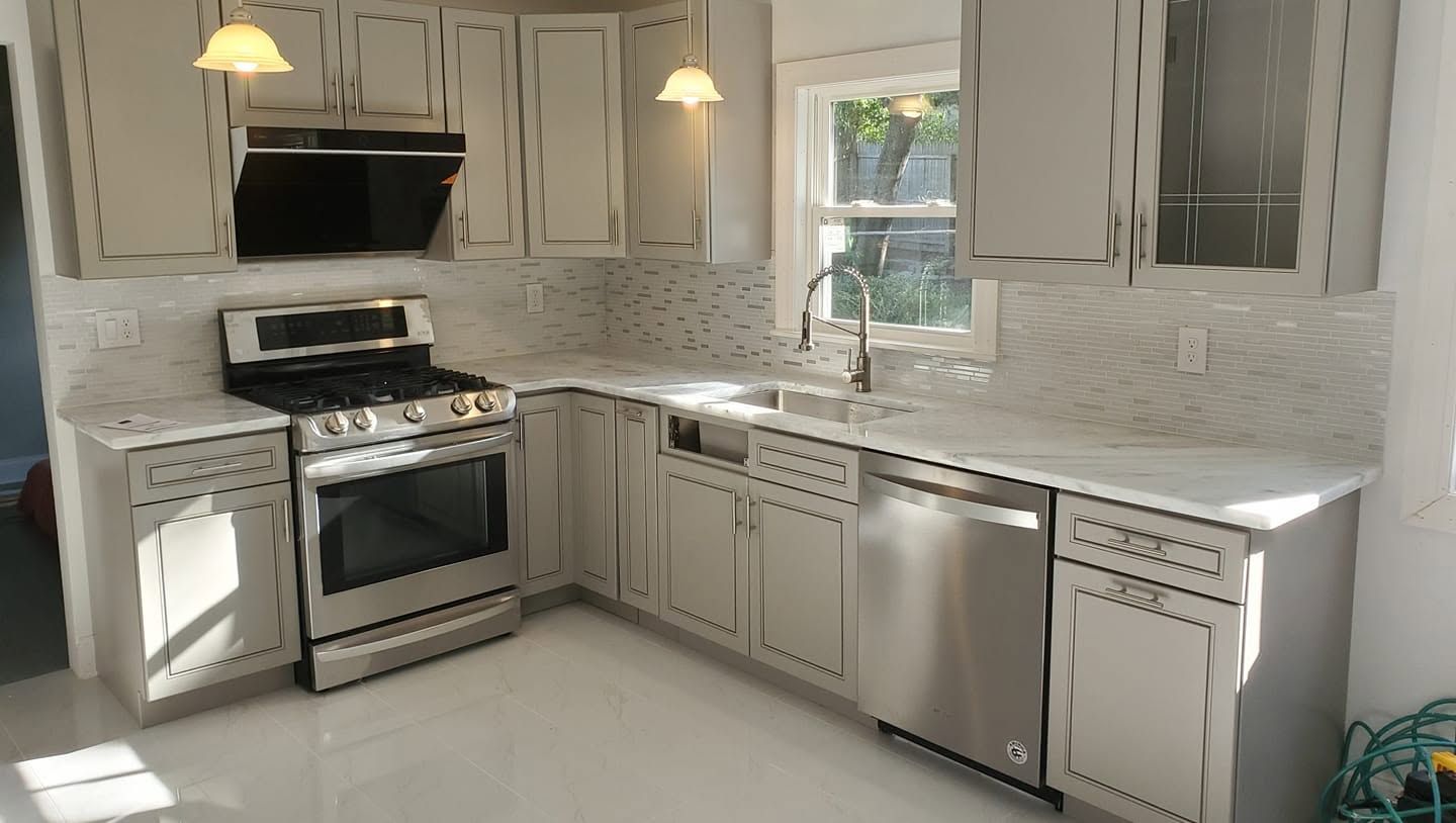 Bright white kitchen with stainless steel stove, dishwasher, cabinets, and sunlit window.