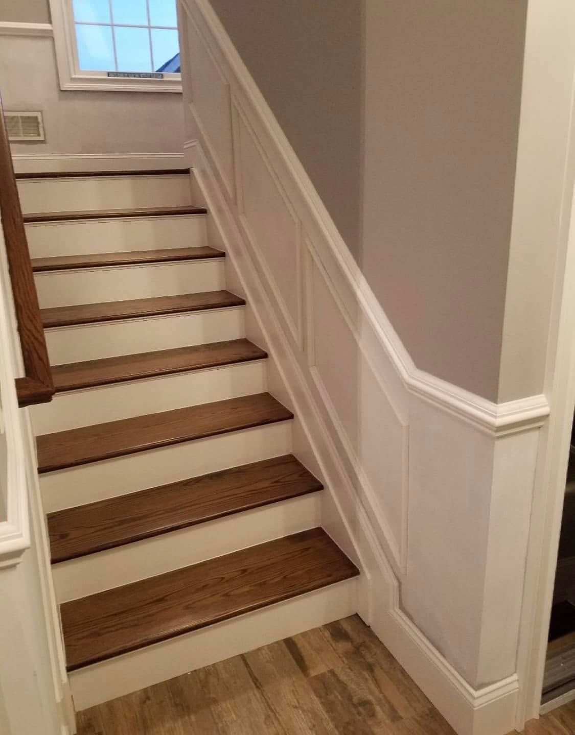 Staircase with white paneling, beige walls, and wood steps beside a hardwood floor hallway.