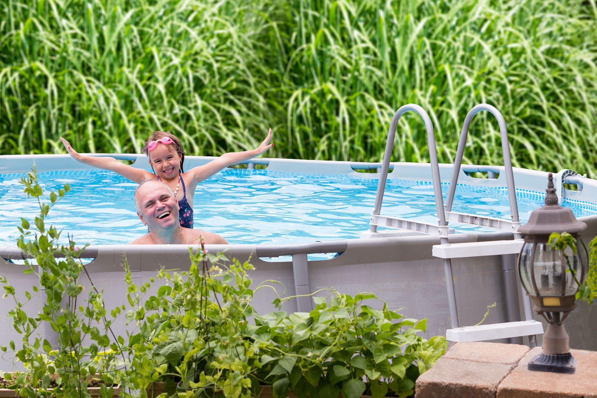 Backyard with a swimming pool, patio furniture, and a house under a bright blue sky.