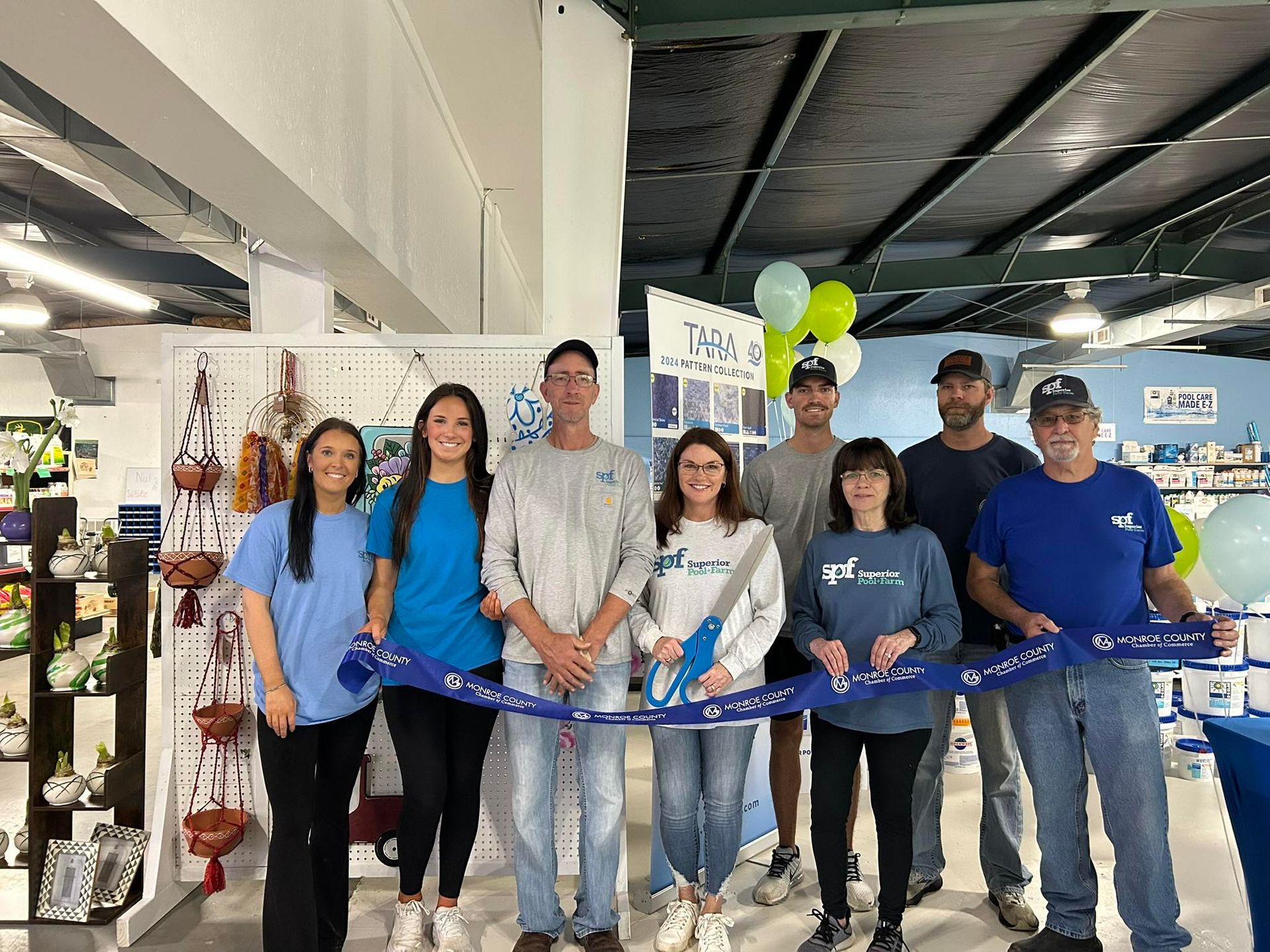 Group of people cutting a ribbon at a store opening; balloons and merchandise in the background.