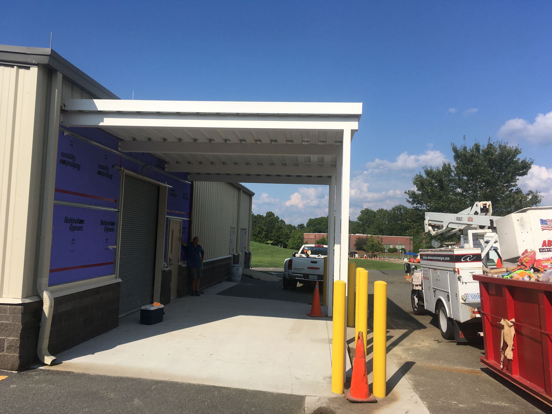 A carport with a white roof is attached to a building under construction. A white truck is visible.