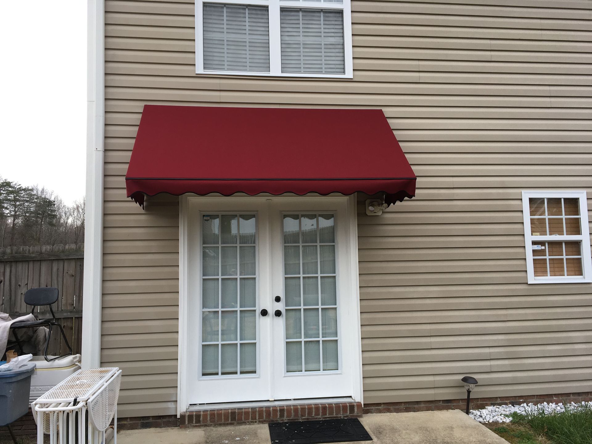 Maroon awning over white French doors on beige siding.
