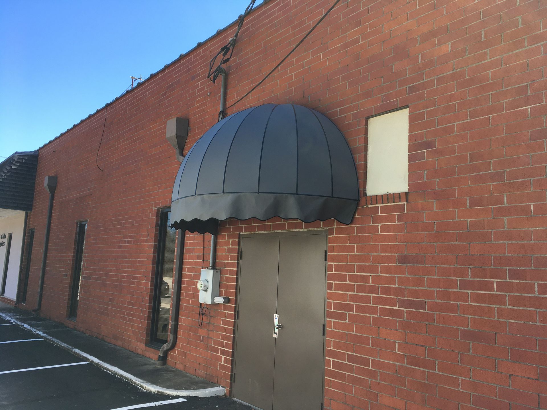 Red brick building with a black dome awning over a brown door.