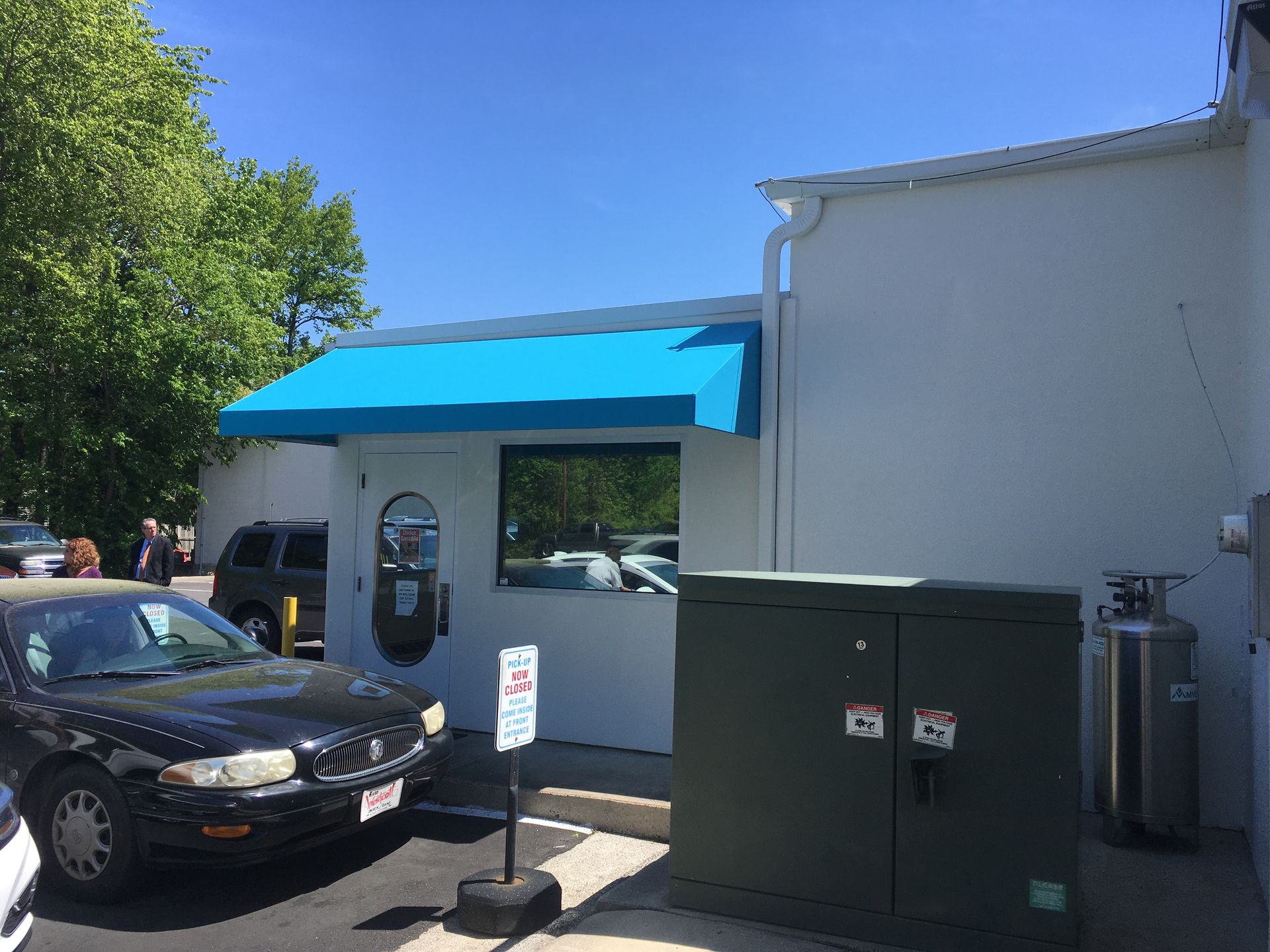 Exterior of a white building with a blue awning over a window. A car is parked in front.