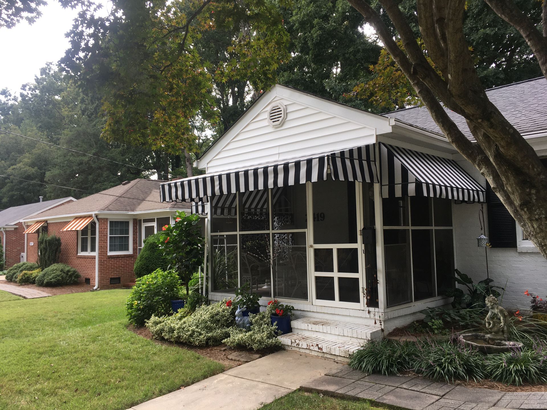 Houses with black and white striped awnings and brick exteriors. Green grass and trees are in the background.