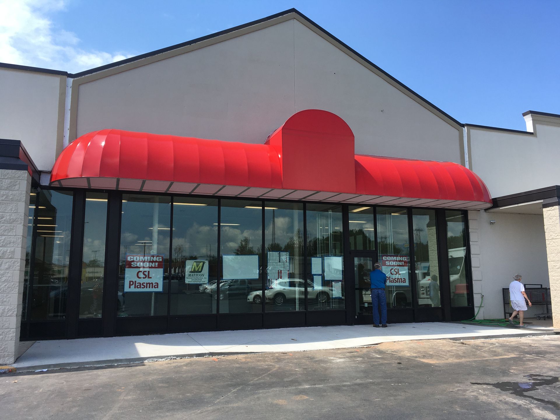 Exterior of store with red awning; a few people outside, glass doors, and a sign.