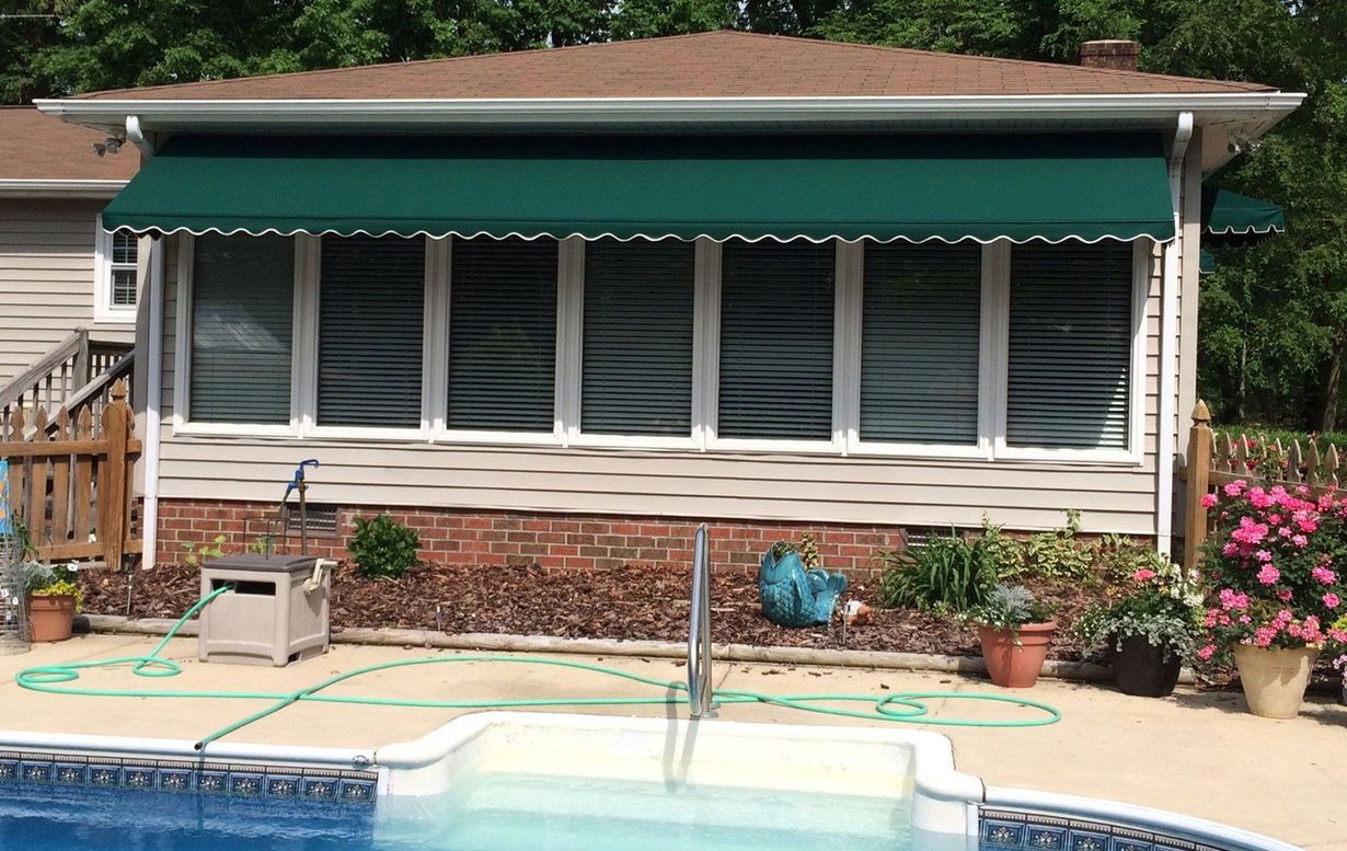 Green awning over windows of a house with a pool in the foreground.