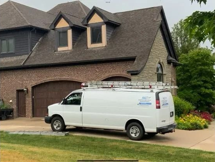 White van with ladder parked in front of a house. Brick, stone, and brown roof.