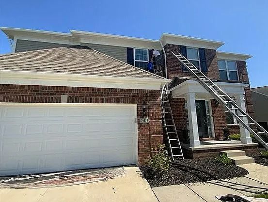 Two-story brick house with a ladder leaning against it. A person is on the ladder, possibly working.