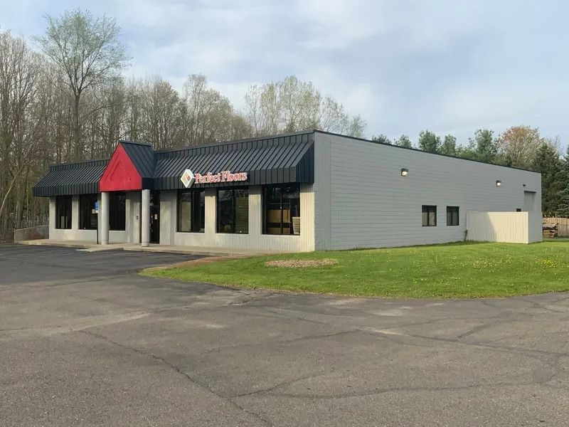 Exterior of Perfect Fitness gym with a red awning over the entrance, gray walls, and a grassy lawn.