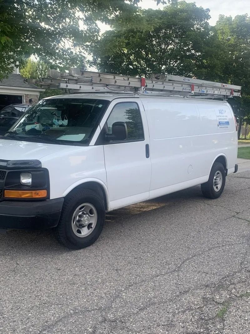 White cargo van with ladder on roof parked on asphalt.