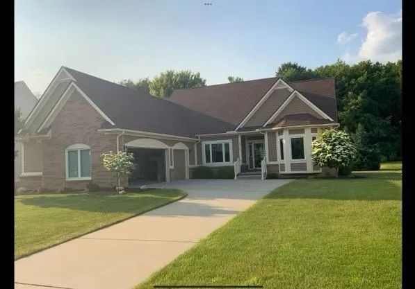 Brick house with brown roof, green lawn, and long driveway.