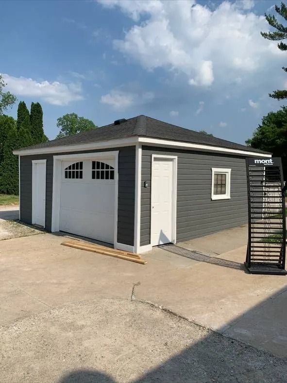 Gray and white garage with a black roof and a concrete driveway on a sunny day.