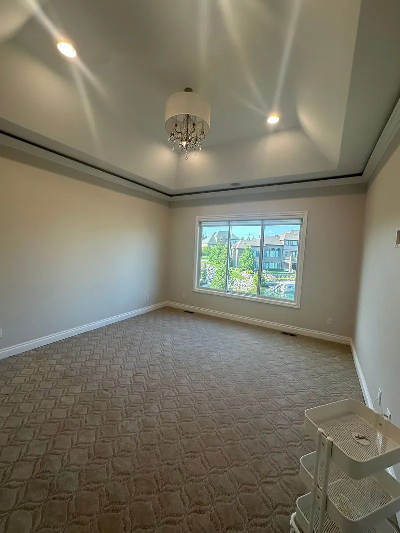 Empty room with patterned brown carpet, large window, and decorative ceiling lights.