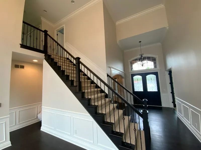 Interior view of a two-story foyer with a dark wood staircase, black railing, and white walls.