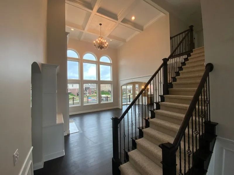 Grand foyer with staircase, dark wood floors, large windows, and coffered ceiling.