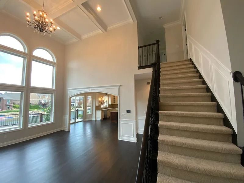 A spacious, two-story interior with dark flooring, staircase, and large arched windows overlooking an outdoor view.