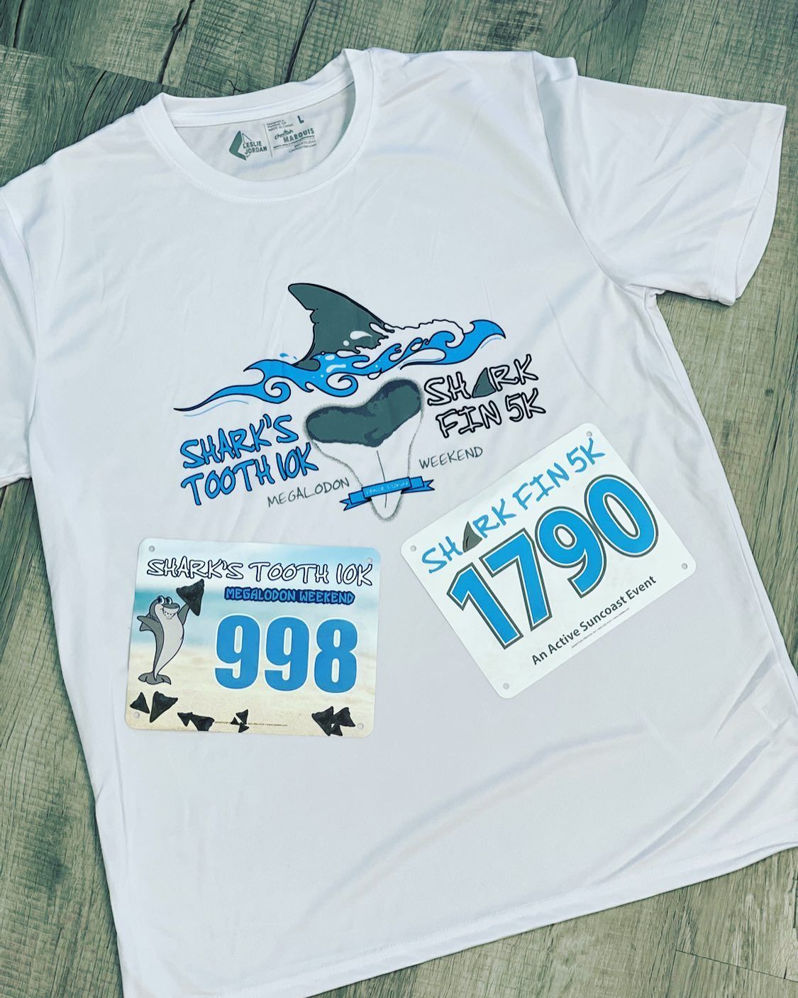 White T-shirt with a shark graphic and blue race-style numbers 998 and 1790 on a green background