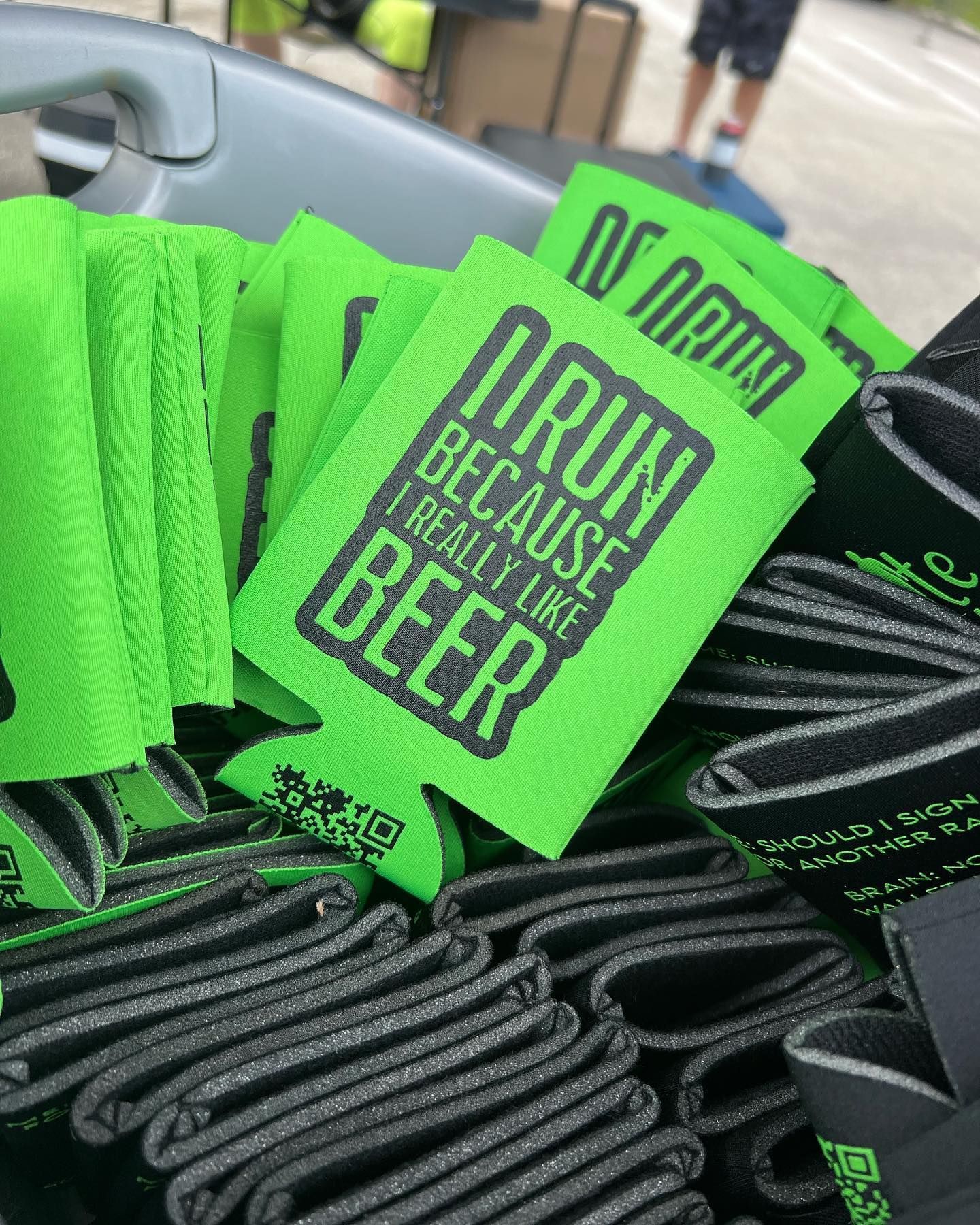 Bright green drink koozies reading “DRINK BEER” and “I DRANK BEER BECAUSE I CAN’T BEER” in a bin