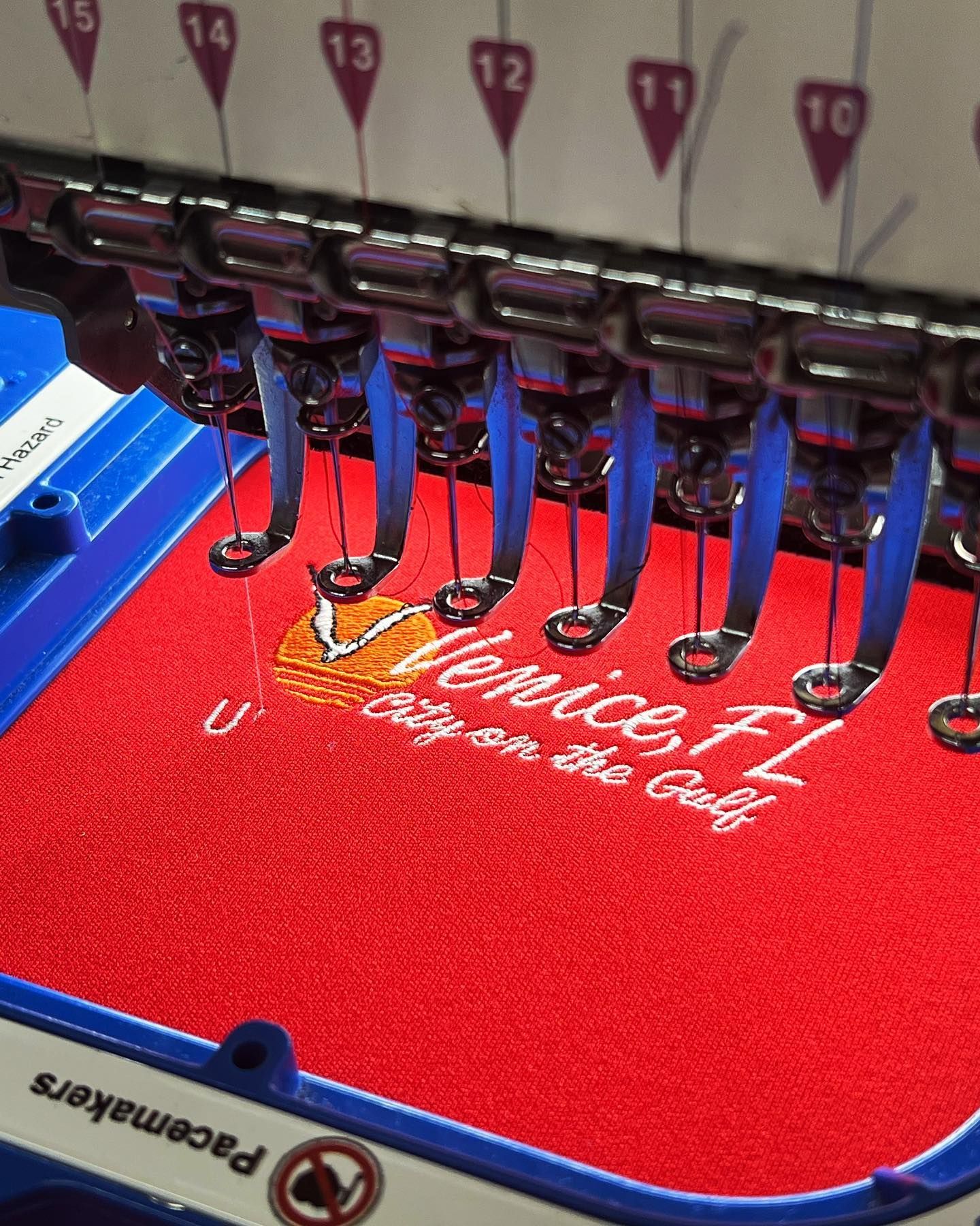 Embroidery machine stitching white script on a red fabric cap with blue trim