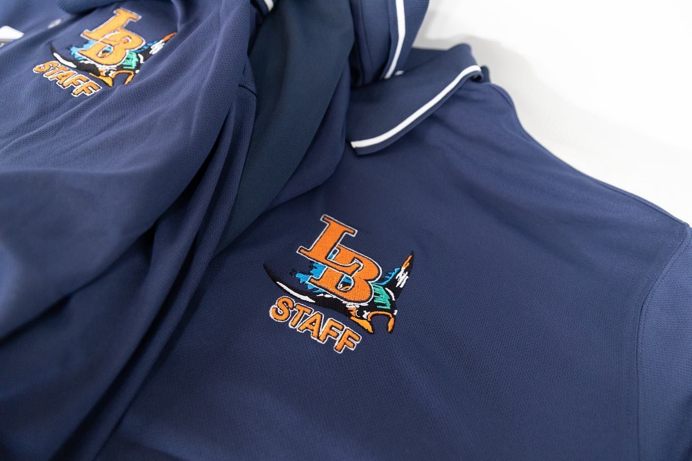 Close-up of navy blue sportswear with an orange-and-blue embroidered logo and white piping.